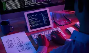 Programista pracuje nad kodem, na ekranie widać tekst i schemat blokowy. H1 html.