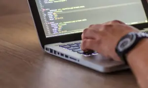 Ręce programisty piszącego kod HTML i CSS na laptopie, optymalizując stronę pod kątem seo.