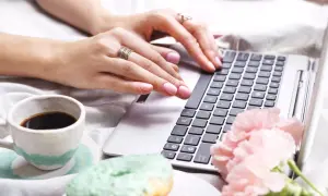 Kobieta pisze na laptopie, obok kawa i pączki. Dowiedz się, jak usunąć twardą spację, by tekst wyglądał idealnie.