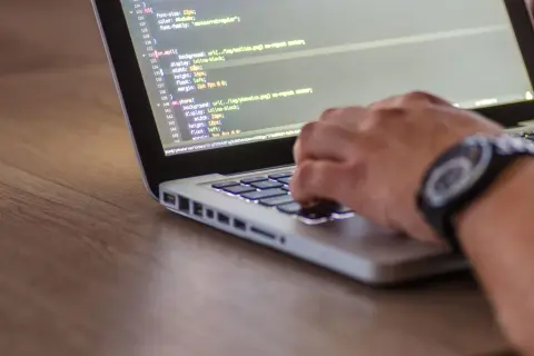 Ręce programisty piszącego kod HTML i CSS na laptopie, optymalizując stronę pod kątem seo.