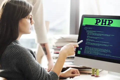 Kobieta z okularami analizuje kod PHP na monitorze. To pokazuje, php do czego służy - do tworzenia stron internetowych.