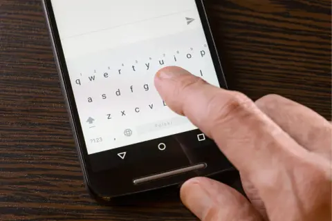 Dłoń pisze na klawiaturze telefonu, ale polskie znaki nie działają. Widoczny przycisk "Polski" sugeruje próbę zmiany języka.