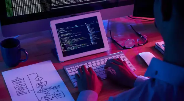 Programista pracuje nad kodem, na ekranie widać tekst i schemat blokowy. H1 html.