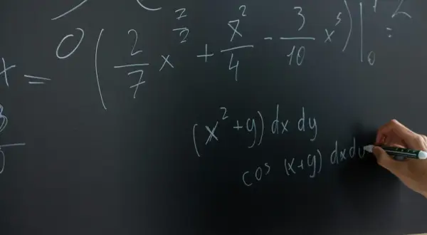 Rysunek przedstawia tablicę z równaniami matematycznymi. Widać całki i wzory, a ręka pisze markerem.