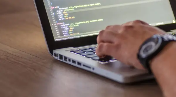 Ręce programisty piszącego kod HTML i CSS na laptopie, optymalizując stronę pod kątem seo.