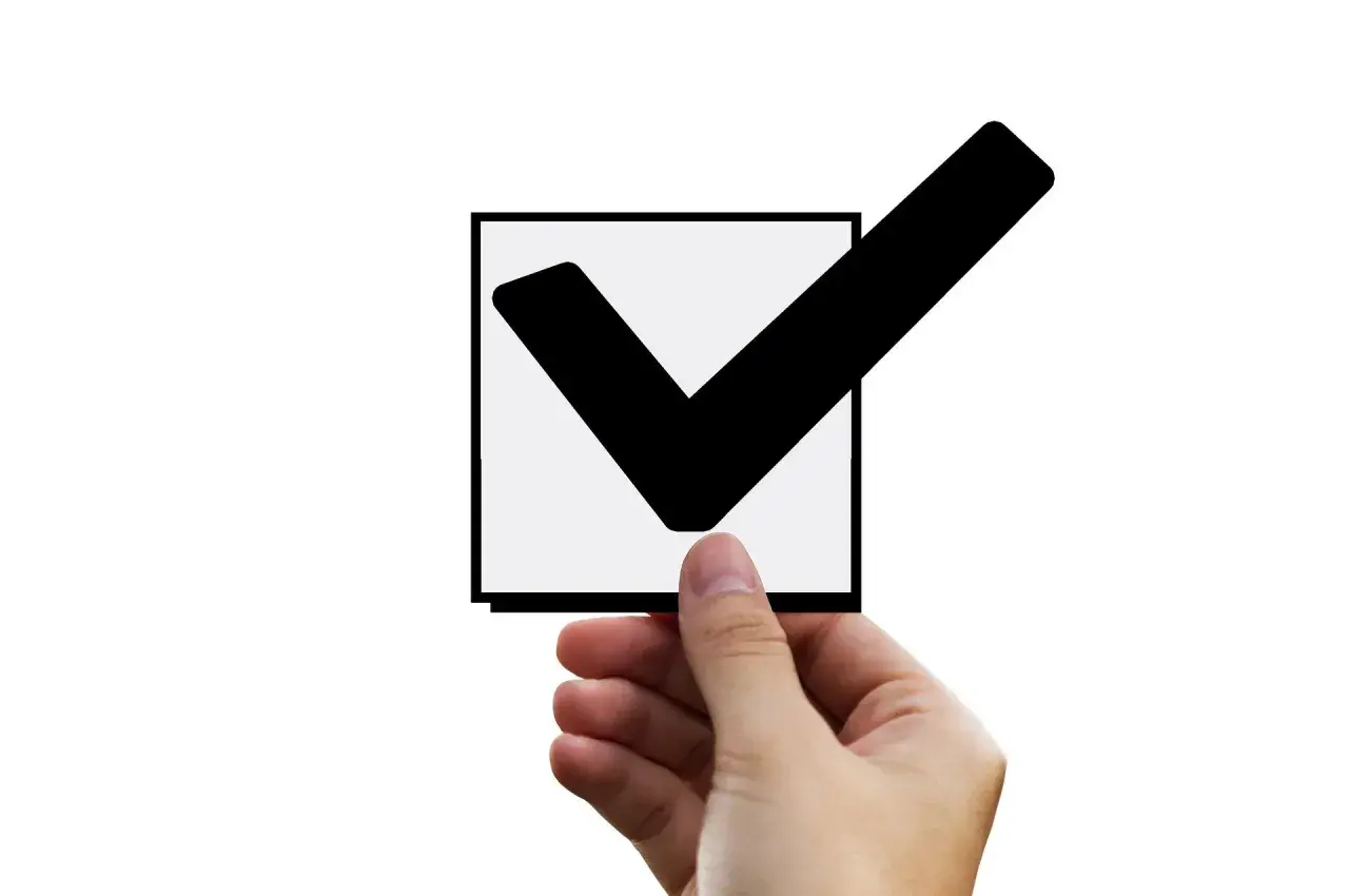 Dłoń trzyma kwadrat z zaznaczonym ptaszkiem. To znak, że input checkbox checked.