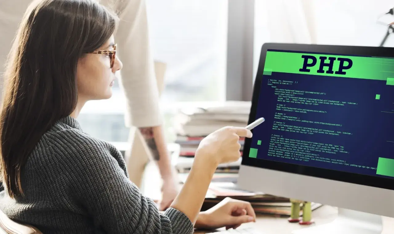 Kobieta z okularami analizuje kod PHP na monitorze. To pokazuje, php do czego służy - do tworzenia stron internetowych.