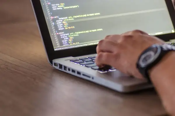 Ręce programisty piszącego kod HTML i CSS na laptopie, optymalizując stronę pod kątem seo.